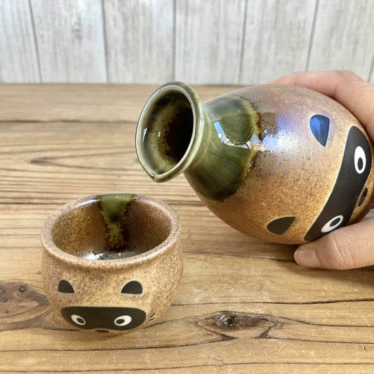 Sake being poured from the Tanuki-themed tokkuri into one of the matching cups, capturing a joyful moment of traditional Japanese sake service