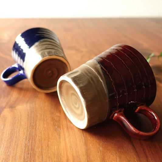 A pair of ceramic mugs with a glossy blue and brown design on a wooden background