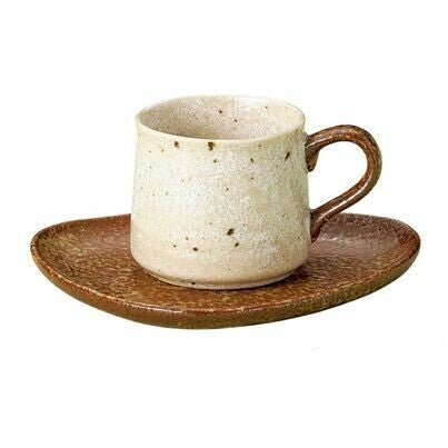 A beige ceramic cup with a soft speckled glaze on a brown saucer, reflecting a wabi-sabi aesthetic with its simple design and natural colors.