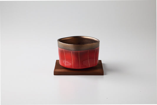 The solid red bowl with gold stripes on a coaster.