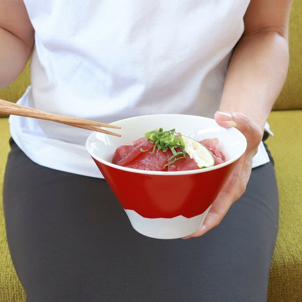 Person holding a mt fuji inspired ceramic bowl of sashimi with chopsticks on a green couch.