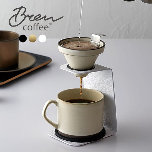 White ceramic dripper and cup set with stainless steel filter and ergonomic handle, resting on modern coffee stand