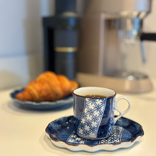 Japanese cup and saucer with a croissant on a kitchen counter.