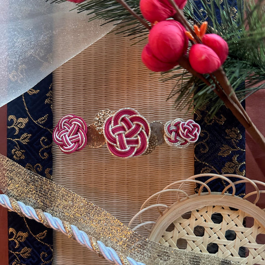 Plum Blossom Knot Barrette in red displayed on a mat, with decorative elements in the background.