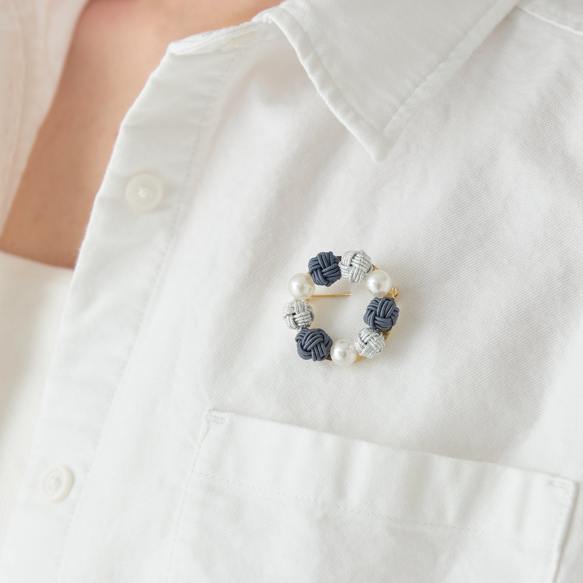 A model wearing a blue handcrafted Mizuhiki brooch with pearl-like beads on a suit