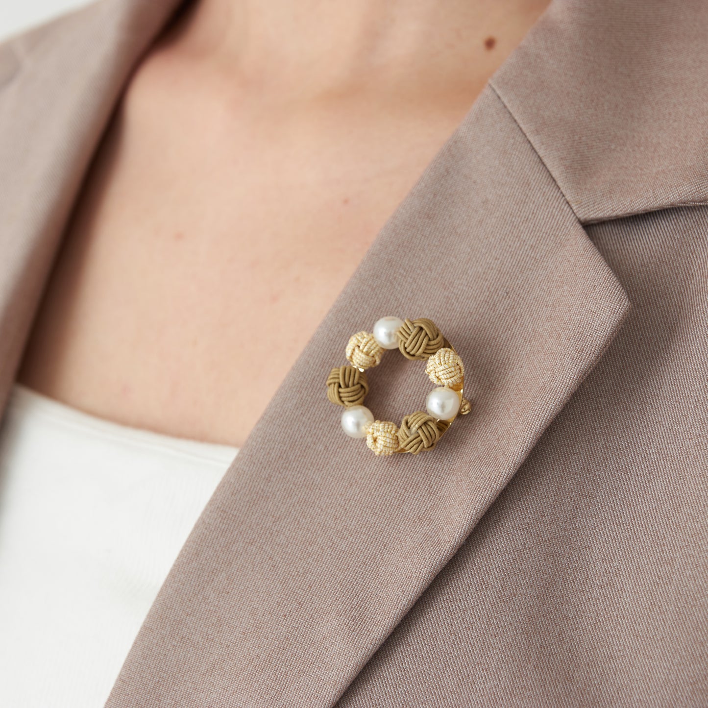 A model wearing a yellow handcrafted Mizuhiki brooch with pearl-like beads on a suit