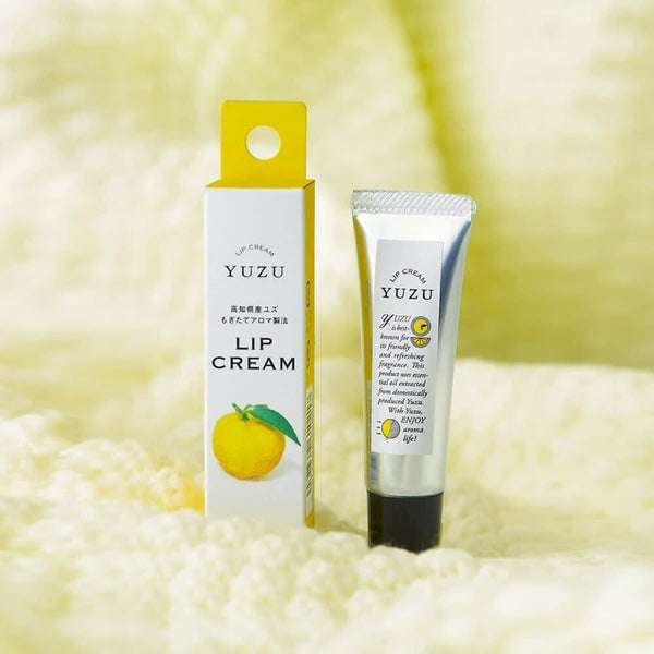 Yuzu lip cream by U&L'VEE, shown with its white and yellow packaging box and a silver squeeze tube with a black cap, set against a soft, textured cream-colored background.