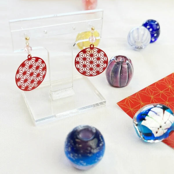 Red hemp leaf earrings displayed on a clear stand with decorative glass balls on a white background