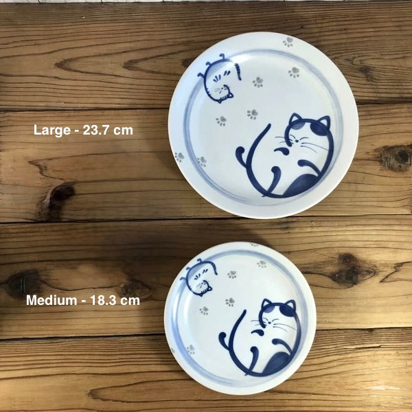 A set of two ceramic plates with a blue cat design on a wooden surface. One large and one medium-sized plate are visible.