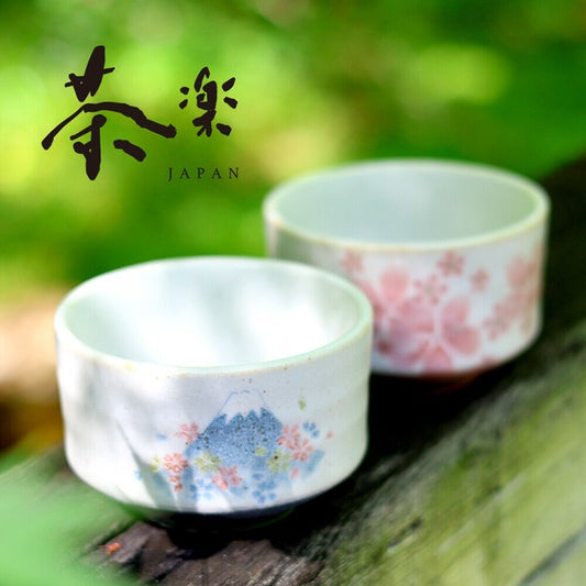 Two Mino Ware matcha bowls with signature Japanese motifs - sakura and Mt Fuji  on a wooden surface with a blurred green background.