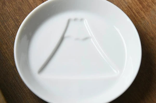 Closer view of white porcelain dipping plate with sauce revealing a Mount Fuji design