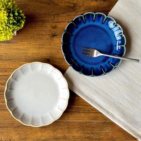 Flower-shaped ceramic plate with deep blue and grey Yūgawari glaze, showcasing soft gradient and petal-like edges on a wooden table 

