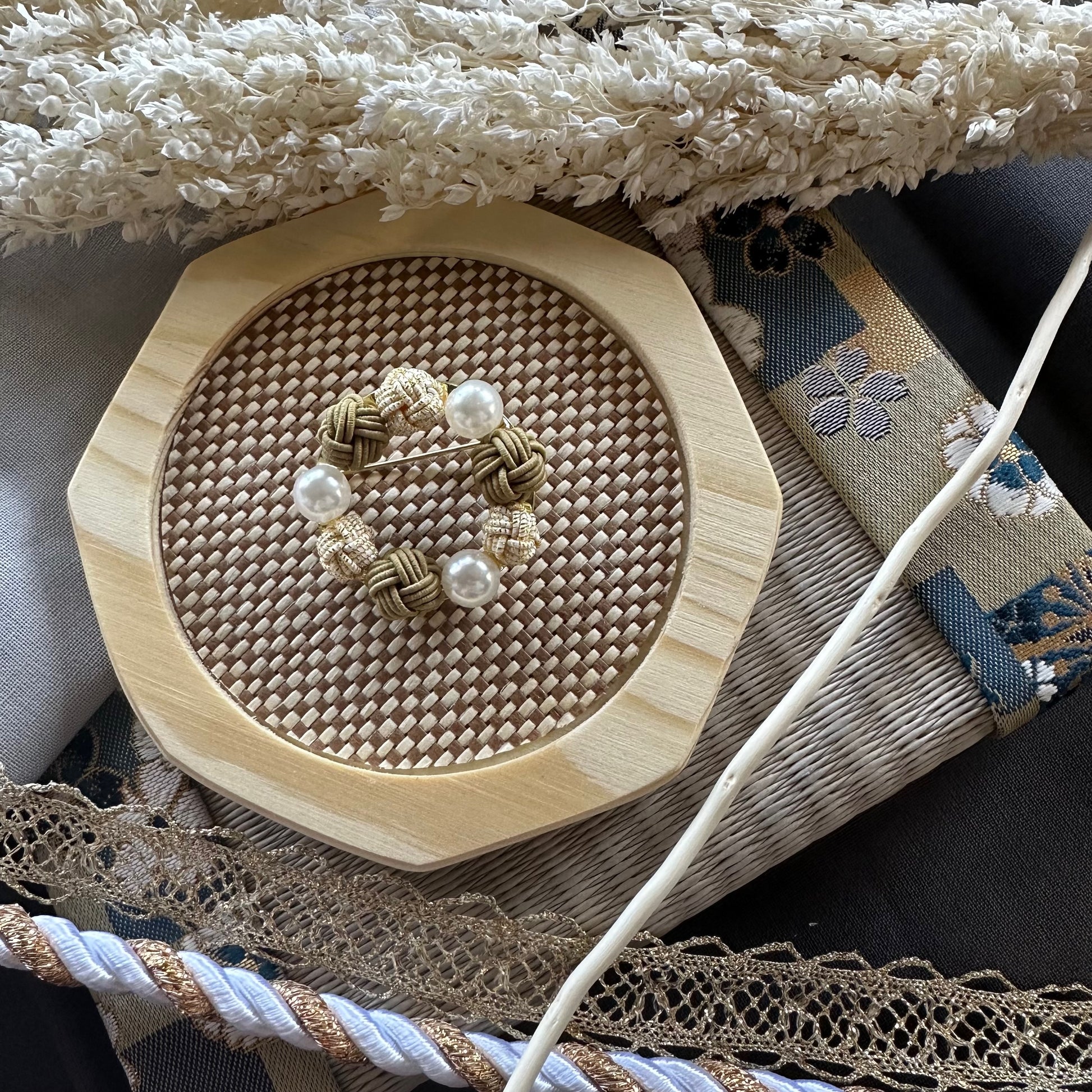 Handcrafted gold Mizuhiki brooch with pearl-like beads displayted on a woven mat