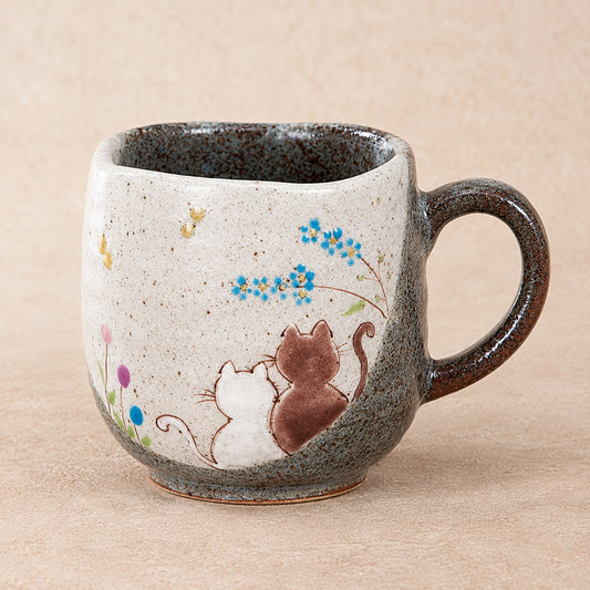 Handmade kutani-ware ceramic mug with a speckled beige and gray exterior, featuring a painted illustration of two small cats and blue flowers, set against a neutral beige background.