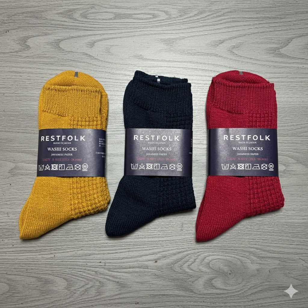 Three pairs of Restfolk wash socks in yellow, black, and red on a wooden surface.